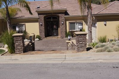 Beige house with stone accents and columns at the entrance, light-colored facade, palm trees, and paved driveway.