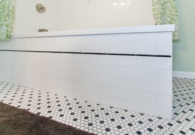 White tiled bathtub front with black accent line, over black and white hexagon floor tiles.