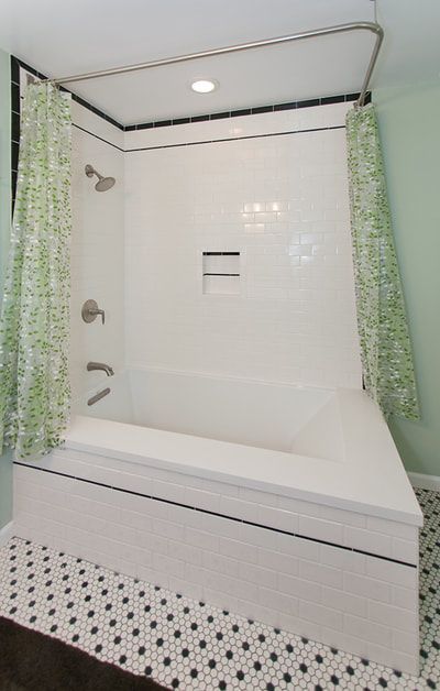 Bathroom with white tiled tub/shower, black trim, green shower curtains, and black and white floor tiles.
