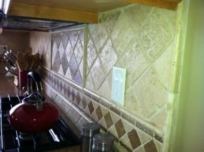 Kitchen backsplash with diamond and square patterned tiles; red teapot on stove.