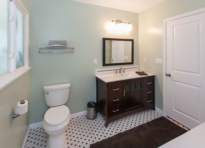 Bathroom with mint walls, dark vanity, white toilet, patterned floor, and a window.