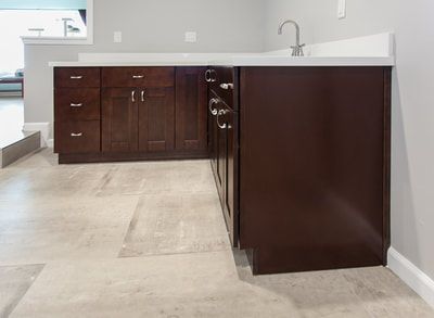 Dark brown cabinets with a white countertop and a sink in a corner kitchen setup.