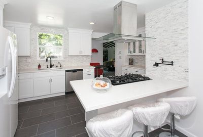 White kitchen with island, gray tile floor, stainless steel appliances and a decorative white stone wall.