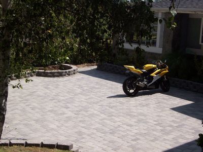 Yellow motorcycle parked on a gray brick driveway in front of a house.