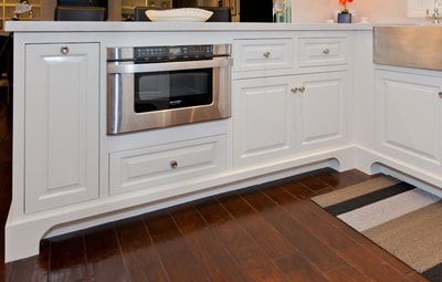White kitchen island with built-in microwave and cabinets on dark wood floor.