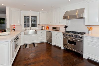 White kitchen with stainless steel appliances, dark wood floor.