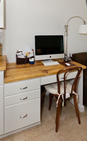 A small home office space with a desk, computer, chair, and lamp.