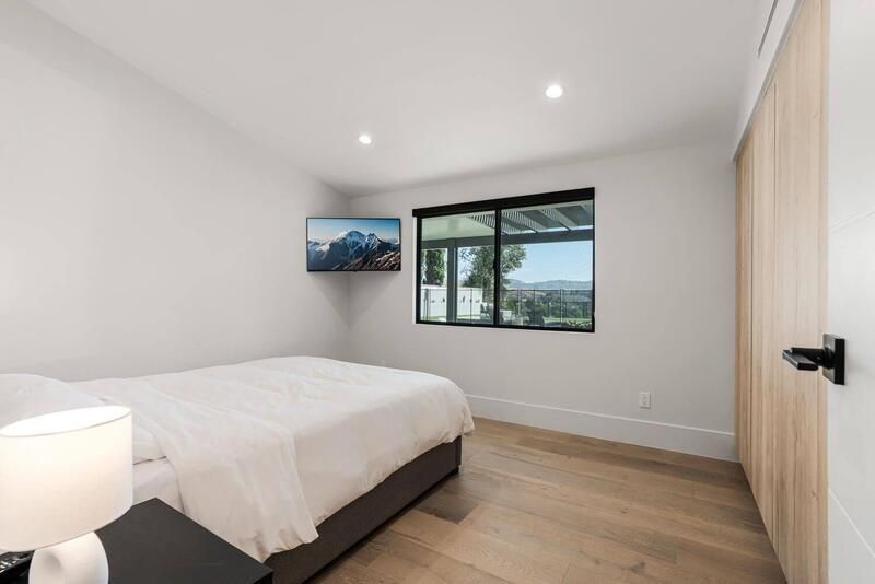 Bedroom with a bed, TV, window with a view, and light-colored wood flooring and door.