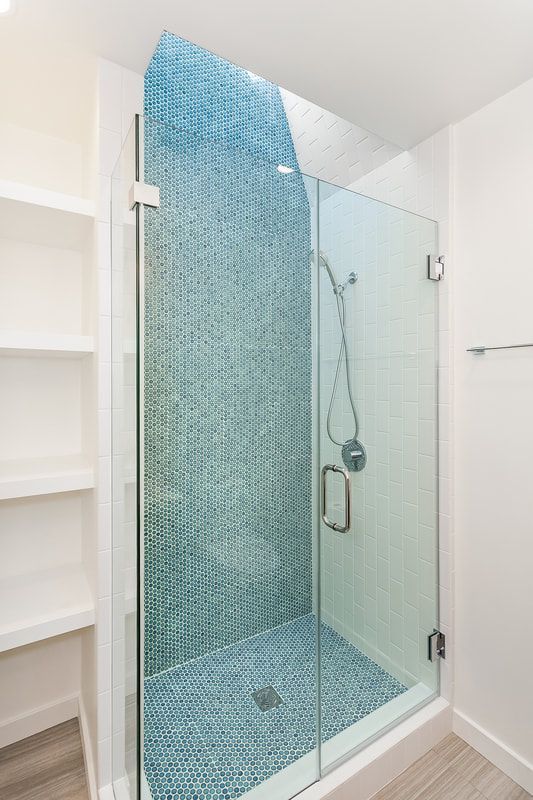 Blue-tiled shower with a glass door, next to a white shelving unit.