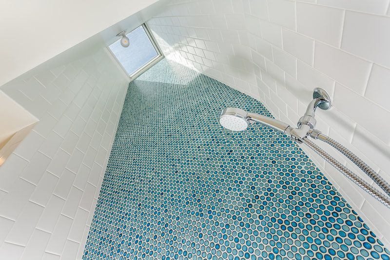 Shower with blue mosaic tile accent wall, white tiles, and skylight.