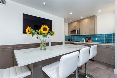 Modern kitchen with white island, stools, sunflowers, and a TV.