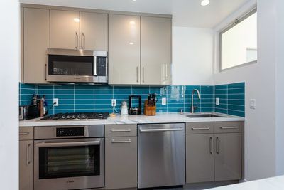 Modern kitchen with gray cabinets, teal backsplash, and stainless steel appliances.