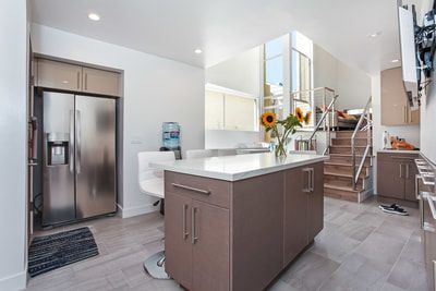 Modern kitchen with stainless steel fridge, island, and a staircase.