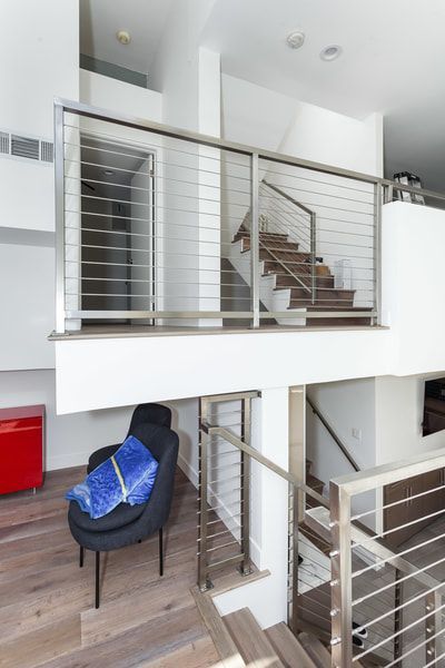 Modern interior with a staircase, stainless steel railings, a chair, and a red cabinet.