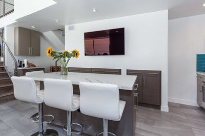 Modern kitchen with island, white chairs, sunflowers, and a wall-mounted TV.