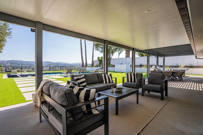 Outdoor patio with modern furniture, city view, swimming pool, and green lawn.