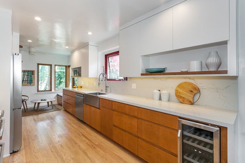 Modern kitchen with white cabinets, wood-tone lower cabinets, stainless steel sink, wine fridge, and light wood floors.