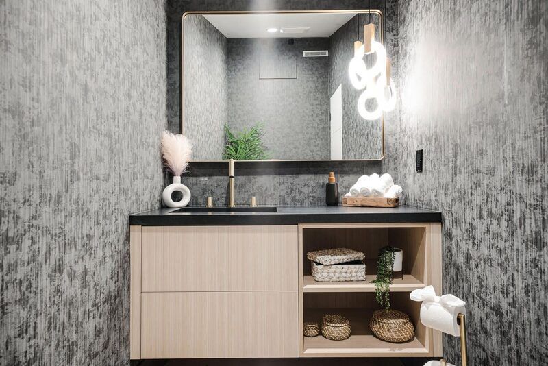 Modern bathroom with wood vanity, black countertop, large mirror, and patterned gray wallpaper.