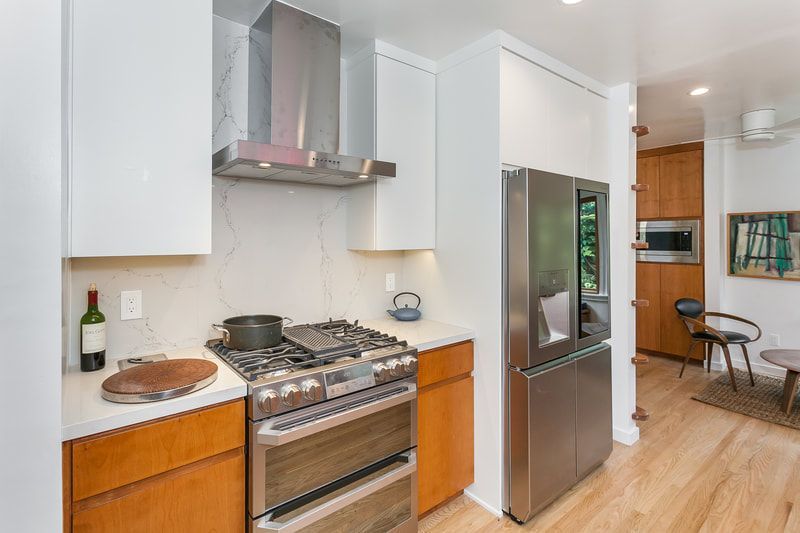 Modern kitchen with stainless steel appliances, light wood cabinets, and white countertops.