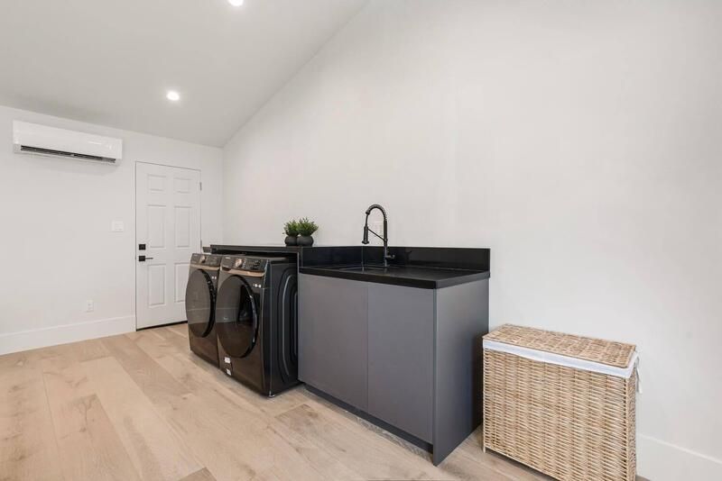 Modern laundry room with black appliances, grey cabinets, a sink, and a wicker hamper.