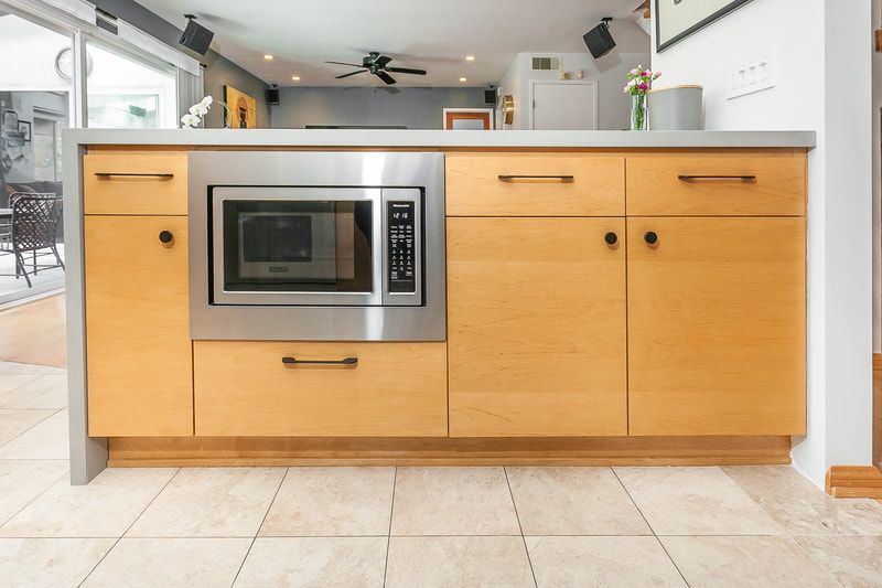 Kitchen island with built-in microwave and light wood cabinets. Stainless steel countertop and appliances.
