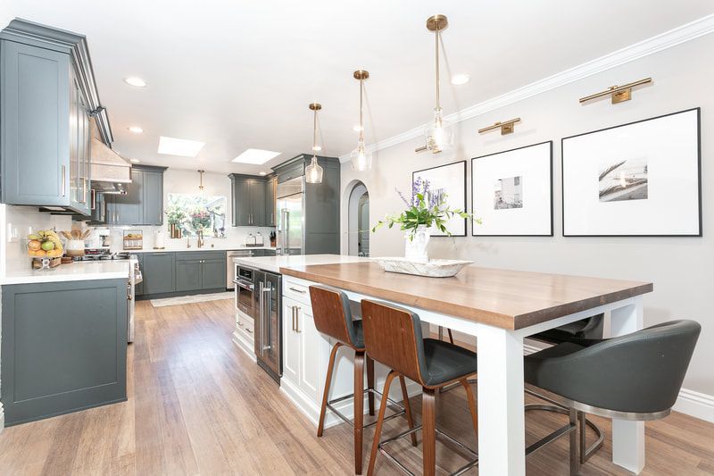 Modern kitchen with gray cabinets, white island with wood countertop, and three framed photos.