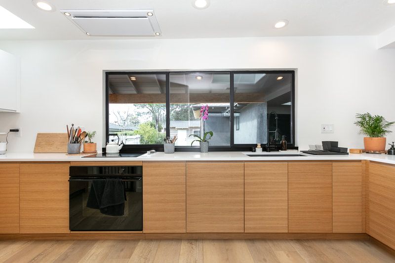 Modern kitchen with light wood cabinets, white countertops, and a large window.