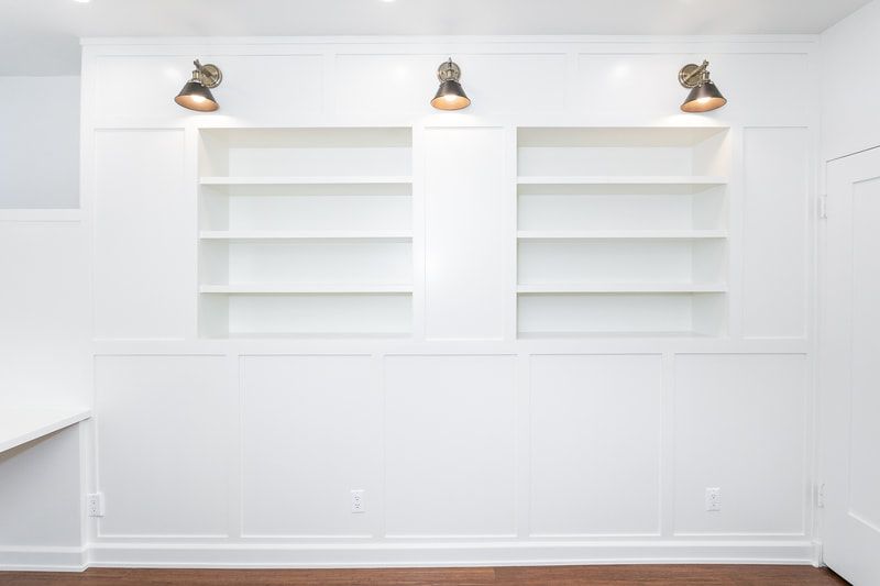 White built-in bookshelves with three spotlights above. The room is painted white.