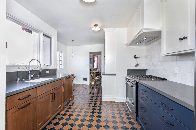 Kitchen with wood and blue cabinets, gray countertops, patterned floor, and white walls.