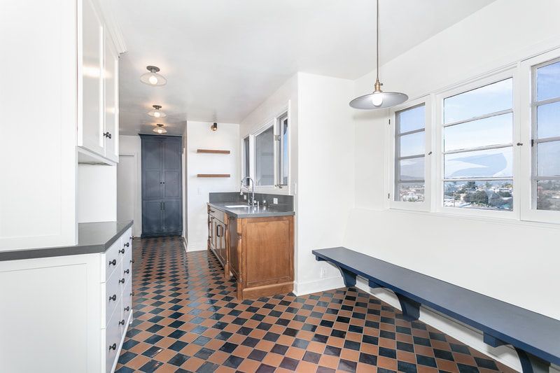 Kitchen with checkerboard floor, wooden cabinets, blue bench by windows.