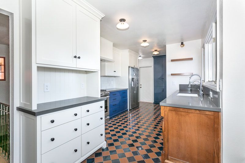 Kitchen with blue and white cabinets, checkered floor, stainless steel appliances, and dark countertops.