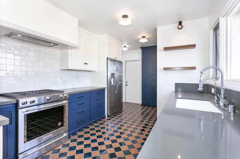 Kitchen with blue cabinets, checkered floor, stainless steel appliances, and gray countertop.