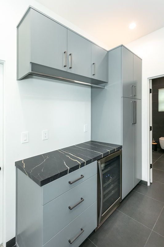 Gray cabinets with black countertop and wine fridge. White walls and dark floor.