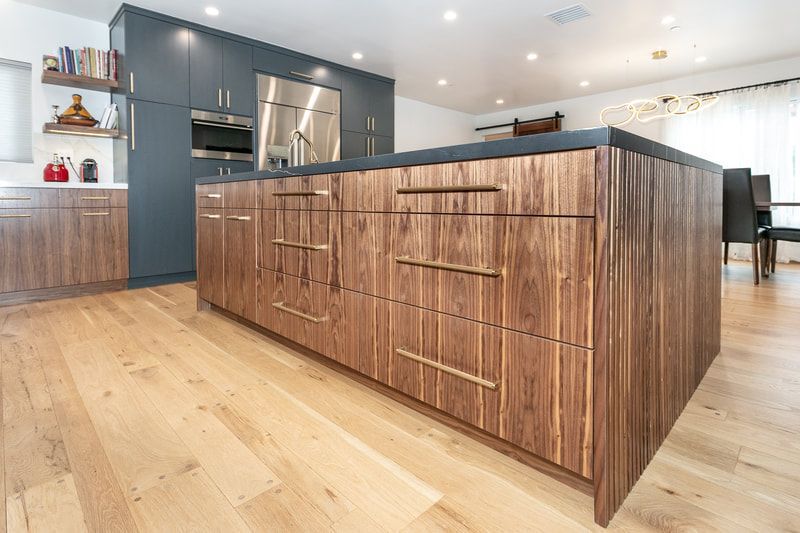 Kitchen island with wood grain cabinets, light wood floor, dark countertops, and blue cabinets.