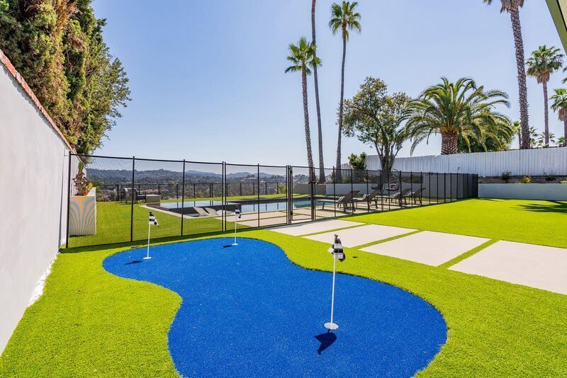 Backyard putting green with pool and palm trees, sunny day.