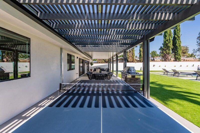 Patio with dark pergola casting shadows, table, grill, and lawn.