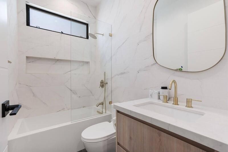 Modern bathroom with marble walls, gold fixtures, and wood vanity.