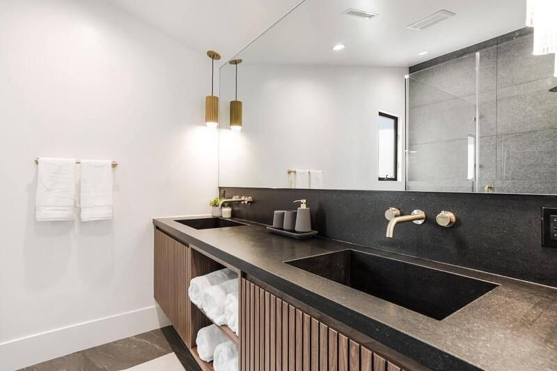 Modern bathroom with double sinks, black countertop, brass fixtures, and pendant lights.