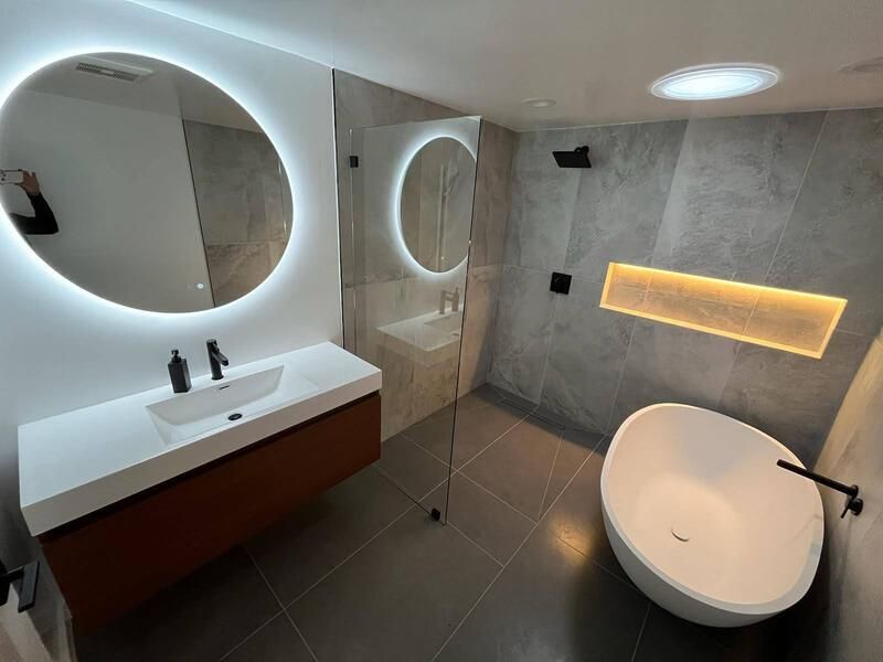 Modern bathroom with a round lighted mirror, floating vanity, and a white freestanding tub.