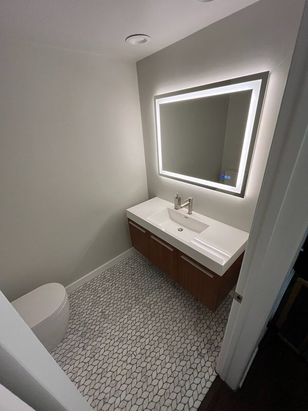 Modern bathroom with floating wood vanity, pebble tile floor, and illuminated mirror.