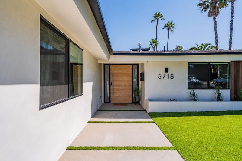 Modern, white house with wooden front door, manicured lawn, and palm trees.