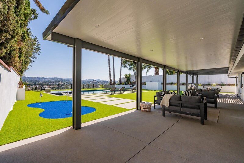 Patio with couches, overlooking a lawn with a pool, green grass, and city view.
