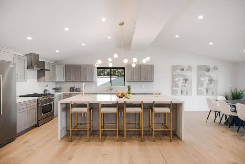 Modern kitchen with island, gray cabinets, gold accents, and a dining area.