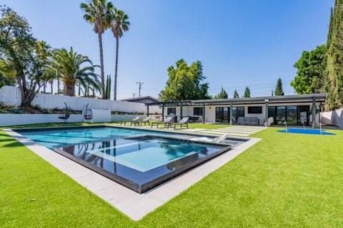 Pool and lounge area in yard with green grass under a clear blue sky.