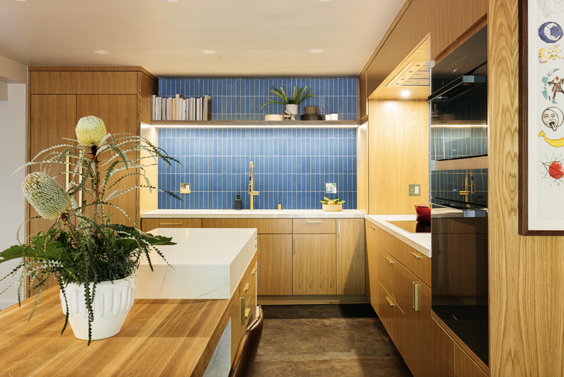 Modern kitchen with light wood cabinetry, blue tile backsplash, and white countertops.