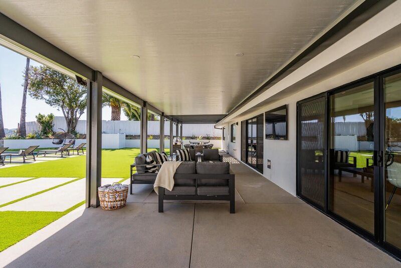 Covered patio with seating, overlooking a green lawn. White and black accents.