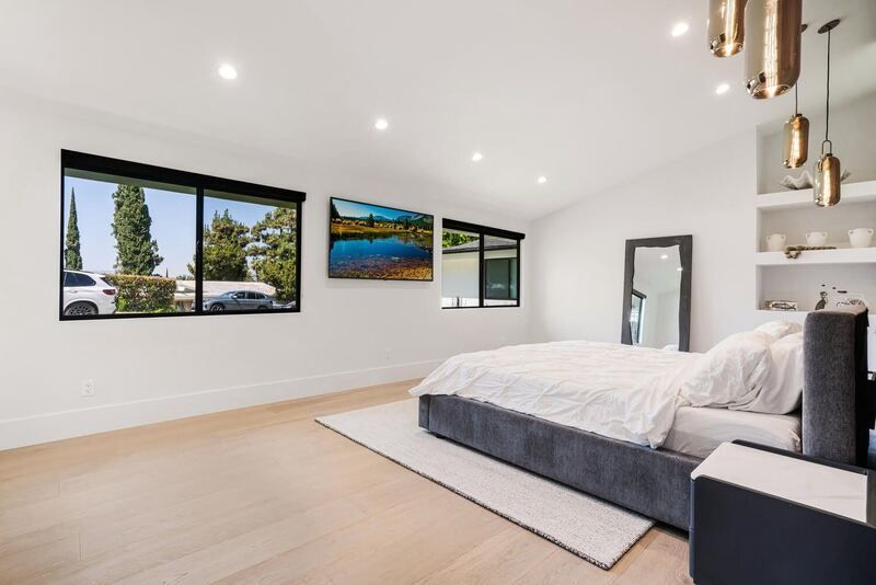 Spacious white bedroom with a bed, windows, a mirror, and recessed lighting.