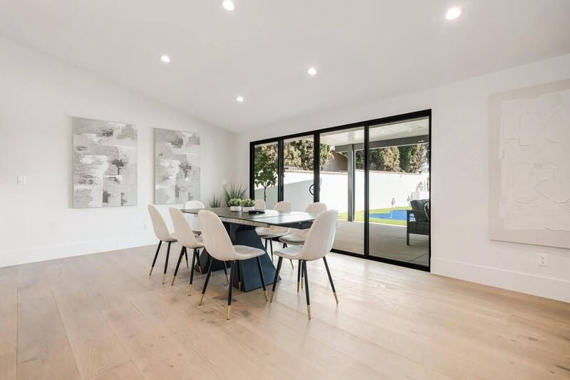 A dining room with a long black table, white chairs, and large sliding glass doors leading to the backyard.