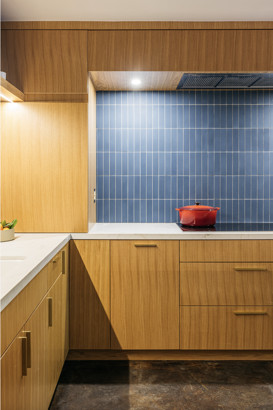 Modern kitchen with light wood cabinets, blue tile backsplash, and a red pot.