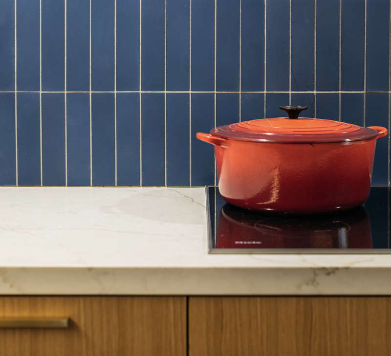 Red pot on a black stovetop, set against a backdrop of blue tiled wall and wooden cabinets.